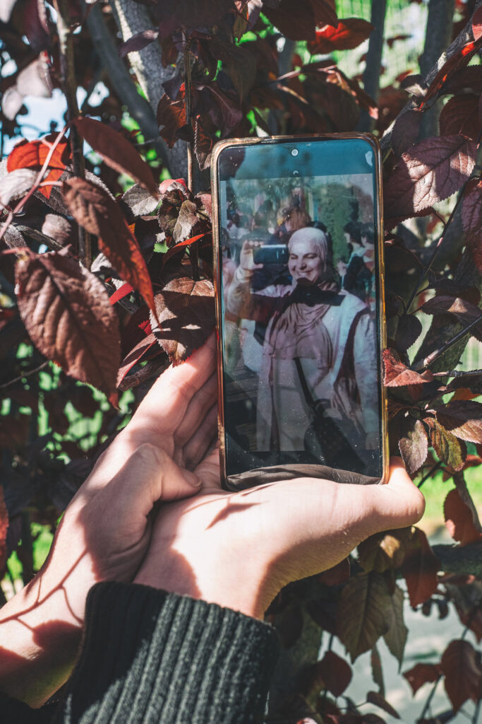 Person holding phone displaying clown image among leaves