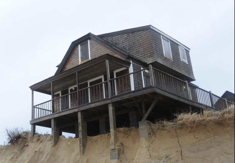 House on stilts above eroding sandy cliff