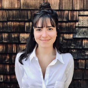 Woman with bun smiling in white shirt by wooden wall