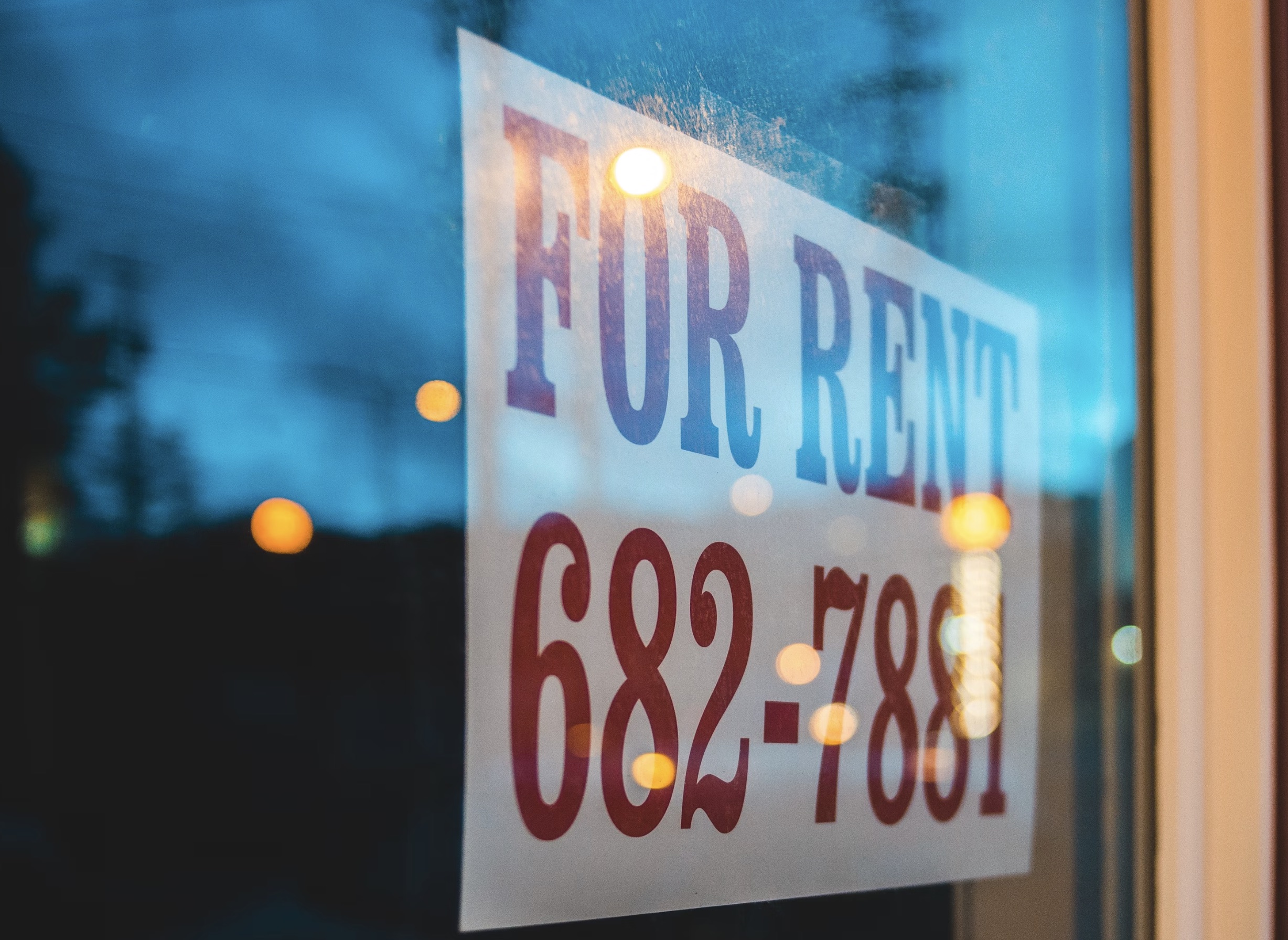 For Rent sign in window at dusk with phone number