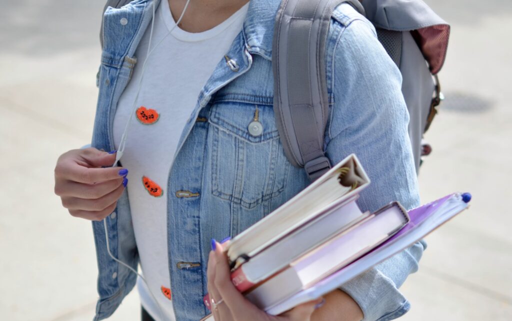 Student holding books, wearing denim jacket and backpack